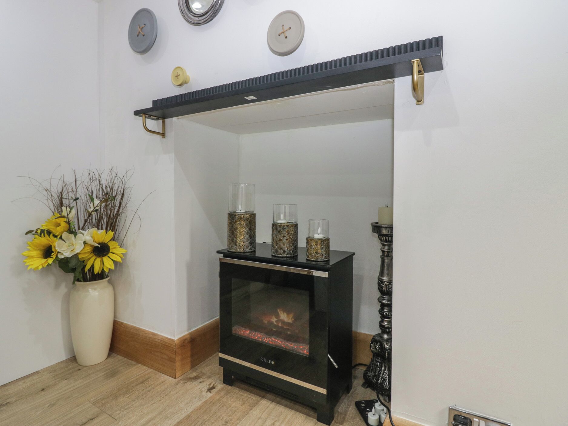 A room with a black wood-burning stove, a white vase with sunflowers, and a wall clock.