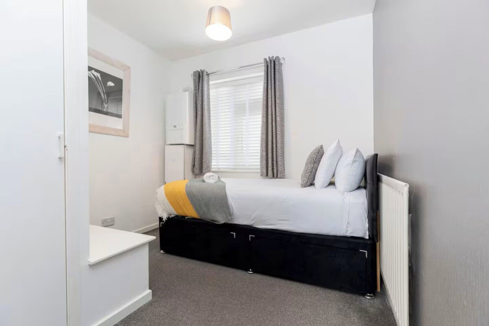 Une chambre à coucher avec un lit, une table de chevet, un radiateur et une fenêtre avec des rideaux.