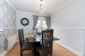 A dining area with a table set for four, a clock on the wall, and a window with curtains.