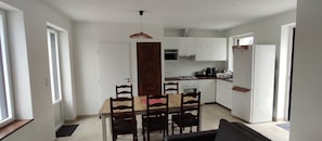 Une cuisine compacte avec des meubles blancs, une table à manger avec des chaises et un luminaire suspendu.