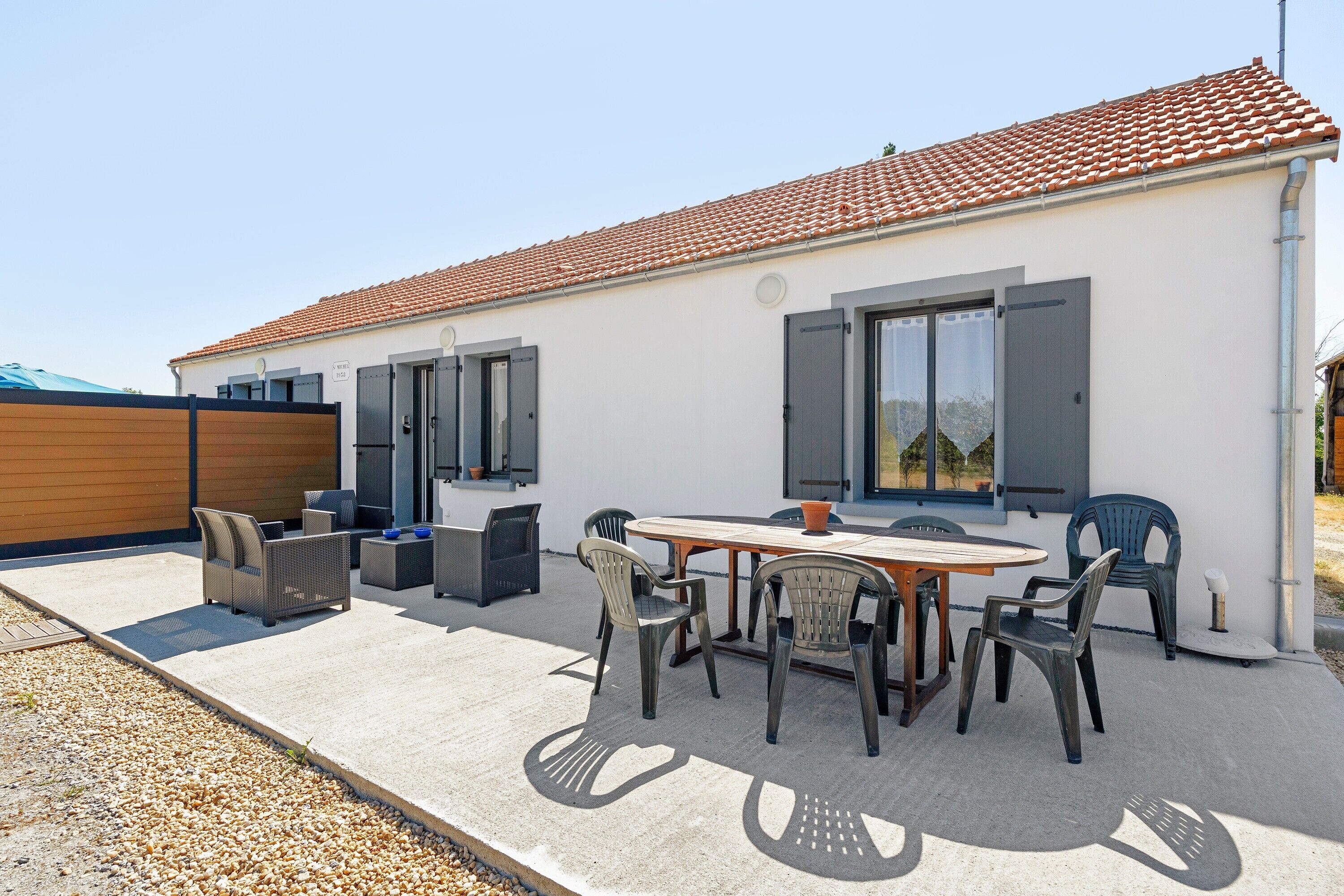 A modern house with a tiled roof, a patio with a table and chairs, and a covered outdoor seating area.