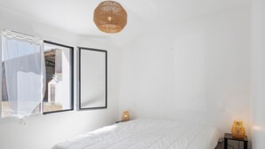 A bedroom with a bed, a window with a sheer curtain, a wall-mounted lamp, and a woven ceiling light fixture. - Family Home for 6–8 Guests with Heated Pool in Vendée! (Commequiers)