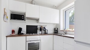 A modern kitchen with white cabinetry, a microwave, stove, oven, and a window providing a view. - Family Home for 6–8 Guests with Heated Pool in Vendée! (Commequiers)