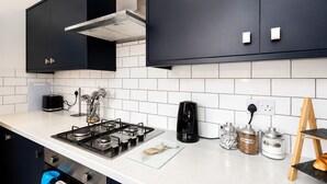 Een moderne keuken met een gasfornuis, een koffiezetapparaat en potten met thee, koffie en suiker.