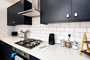 A modern kitchen with a gas stove, a coffee maker, and jars labeled tea, coffee, and sugar. - Modern 4BR Contractor Stay in Darlington (Darlington)