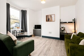 A modern living room with a green sofa, a dining area with a table and chairs, a flat-screen TV, and a wall-mounted shelf with decorative items. - Modern 4BR Contractor Stay in Darlington (Darlington)