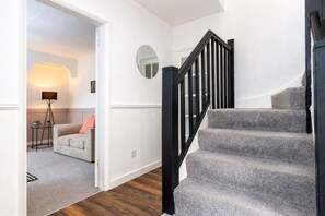 A staircase with a black railing leading to an upper floor, a round mirror on the wall, and a doorway leading to a living area with a sofa and a lamp. - Modern 4BR Contractor Stay in Darlington (Darlington)