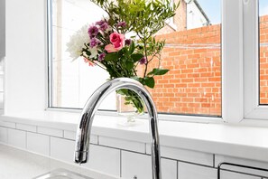 A kitchen with a stainless steel faucet, a window with a view of a brick wall, and a vase with flowers on the windowsill. - Modern 4BR Contractor Stay in Darlington (Darlington)