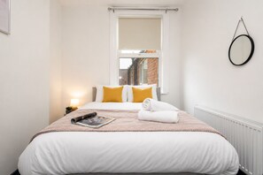 A neatly made bed with white bedding and two yellow pillows, a rolled white towel, and a magazine on the bed.