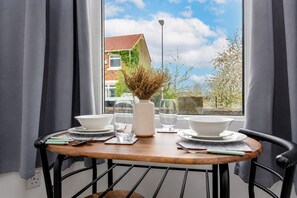 A dining table with white plates, bowls, and glasses, a vase with dried plants, and a window with a view of a building and trees. - Modern 4BR Contractor Stay in Darlington (Darlington)