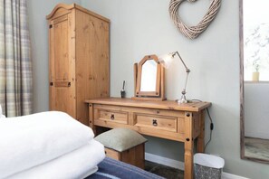 Ein Schlafzimmer mit einem Holzkapuzen-Kommode, einem Spiegel, einer Lampe, einem Bett und einem Korbgirlanden an der Wand.