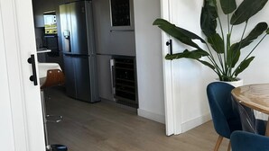Moderni keittiö, jossa on ruostumattomasta teräksestä valmistetut kodinkoneet, ruokailutila pöydän ja tuolien kera sekä suuri kasvi.