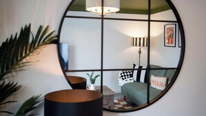 Une pièce avec un grand miroir rond qui reflète un canapé vert, une lampe et un tableau encadré accroché au mur.