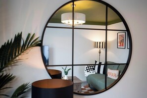 Ein Zimmer mit einem runden Spiegel, der ein grünes Sofa, eine Lampe und ein gerahmtes Bild an der Wand reflektiert.