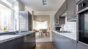 A modern kitchen with dark cabinets, a marble countertop, and a view into the dining area. - 4BR Contractor Stay | Parking, Wi-Fi, Spacious (Sunderland)