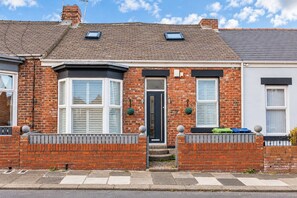 A two-story brick house with a bay window, a front door, and a small porch area.