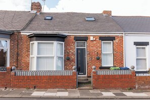A two-story brick house with a bay window, a front door, and a small porch area.