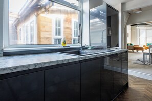 Eine moderne Küche mit großem Fenster, dunklen Schränken und einer Marmorarbeitsplatte.