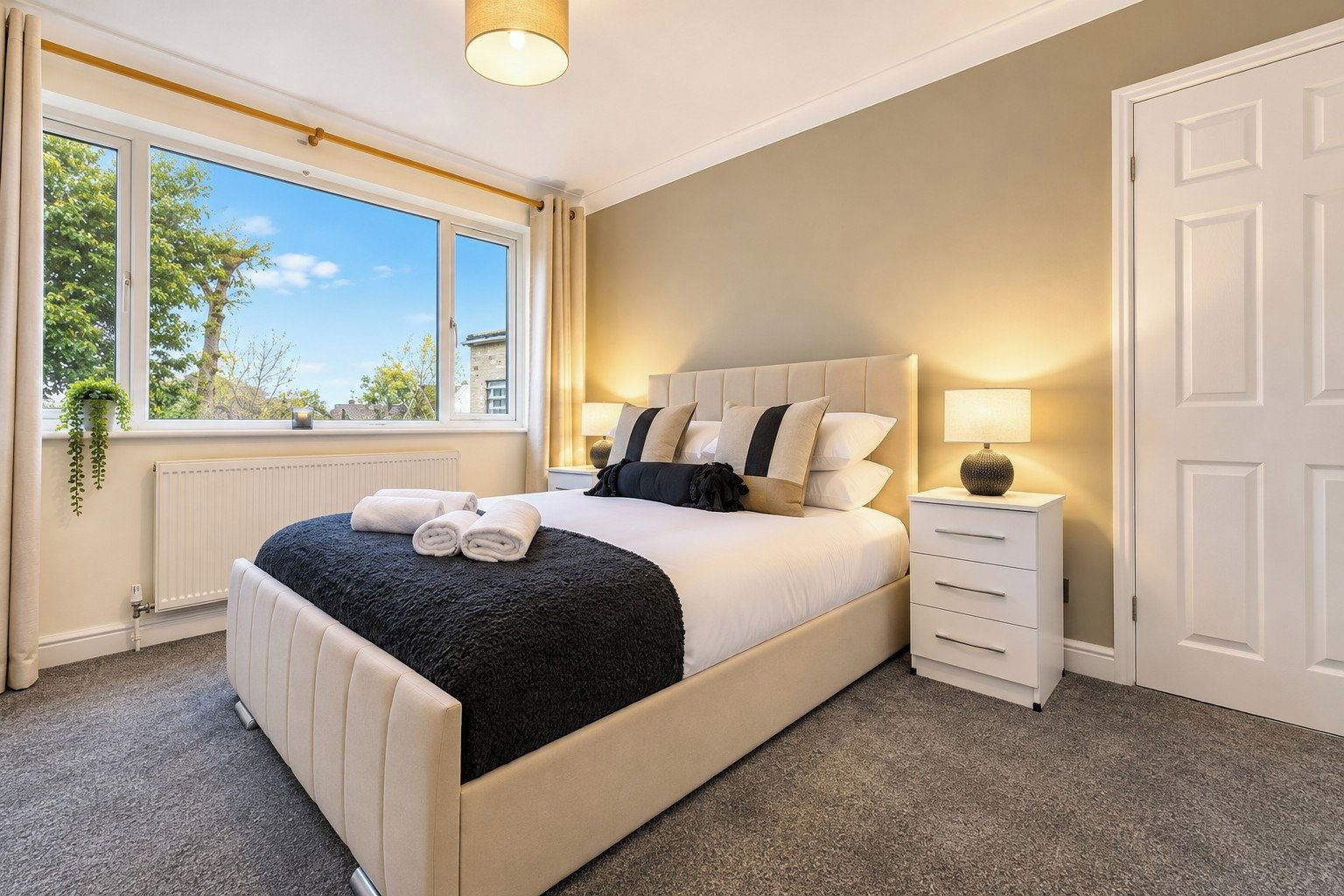 Une chambre d’hôtel avec un grand lit, une table de chevet, une lampe et une vue sur l’extérieur.