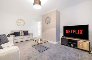 A living room with a sofa, coffee table, TV, and a wall clock. - Modern 2BR | Middlesbrough | Parking (Normanby)