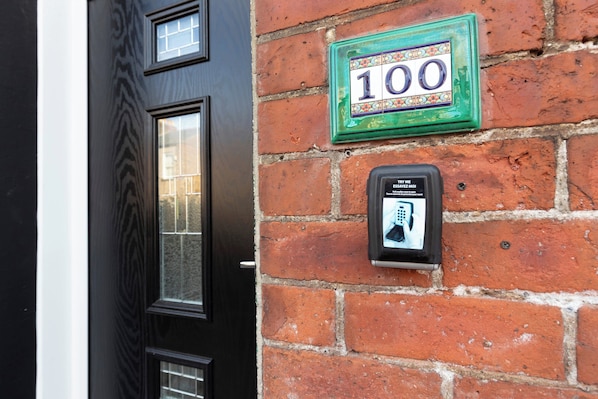 A brick wall with a numbered plaque and a security intercom.