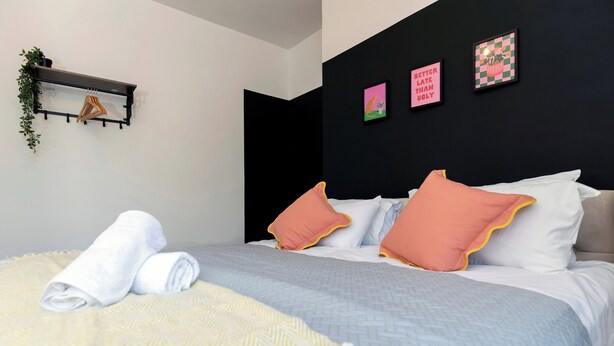 A neatly made bed with pillows, a towel, and a blanket. There is a shelf with plants and a picture frame on the wall. - Spacious 3BR • WiFi • Parking • Contractor Stay (Sunderland)