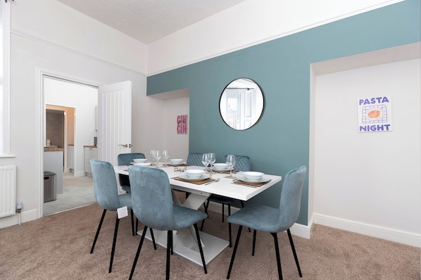 A dining area with a white table set for four, light blue chairs, and a mirror on the wall. - Spacious 3BR • WiFi • Parking • Contractor Stay (Sunderland)