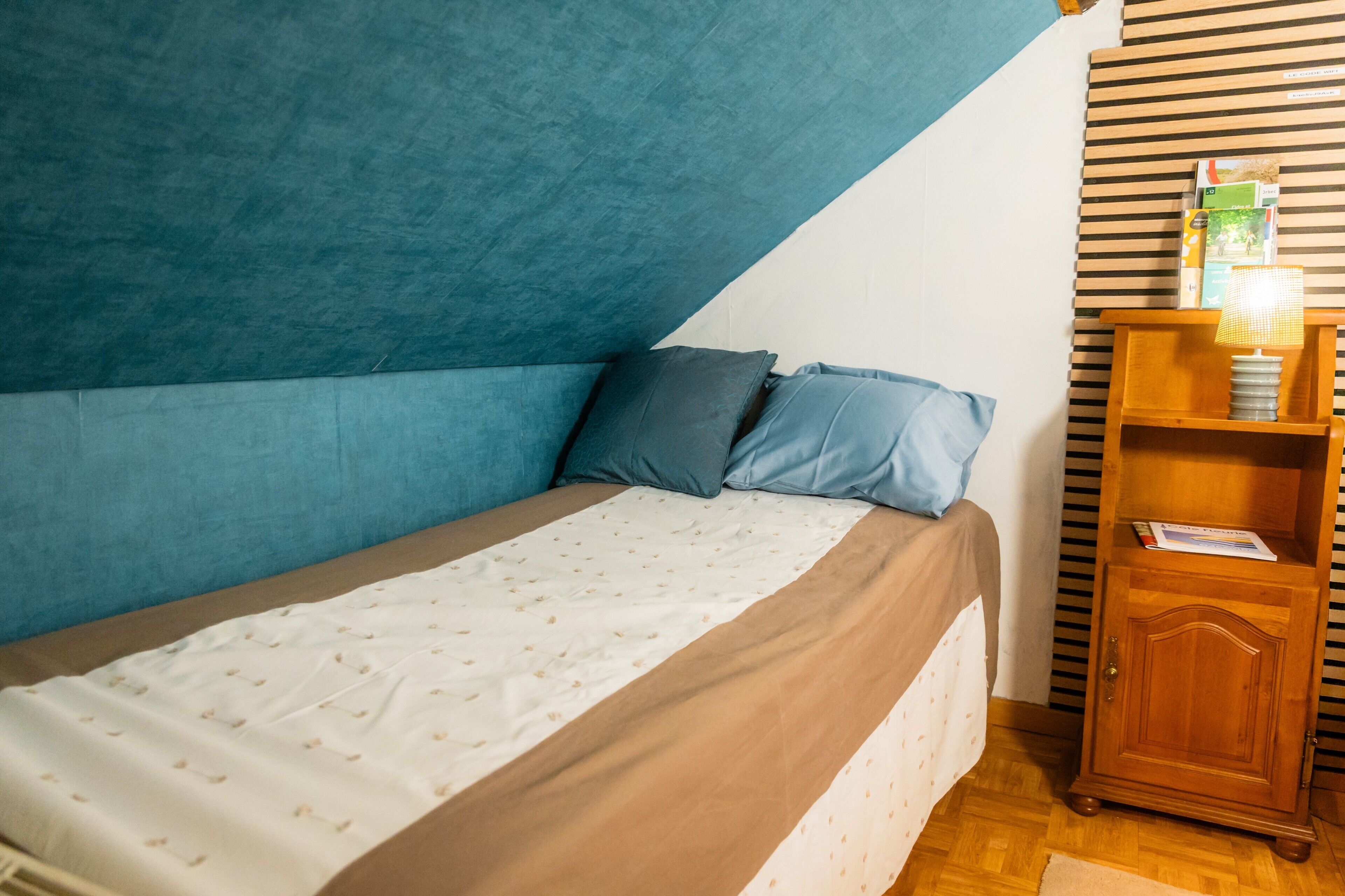 Un dormitorio con una cama, almohadas, una mesita de noche de madera y una pared a rayas.