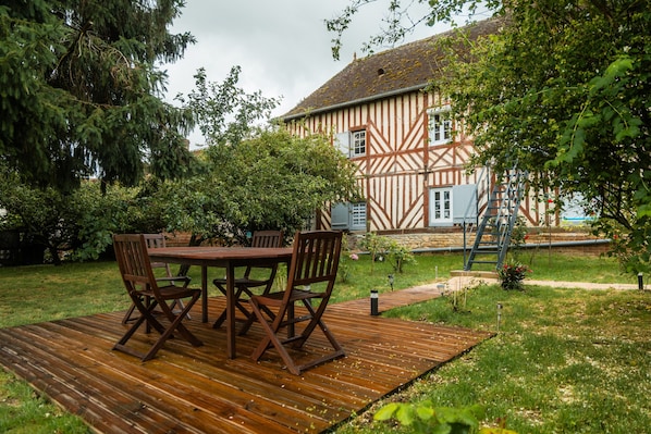 Une maison traditionnelle à colombages, dotée d’une terrasse en bois, d’une table avec des chaises et d’une échelle menant au toit.