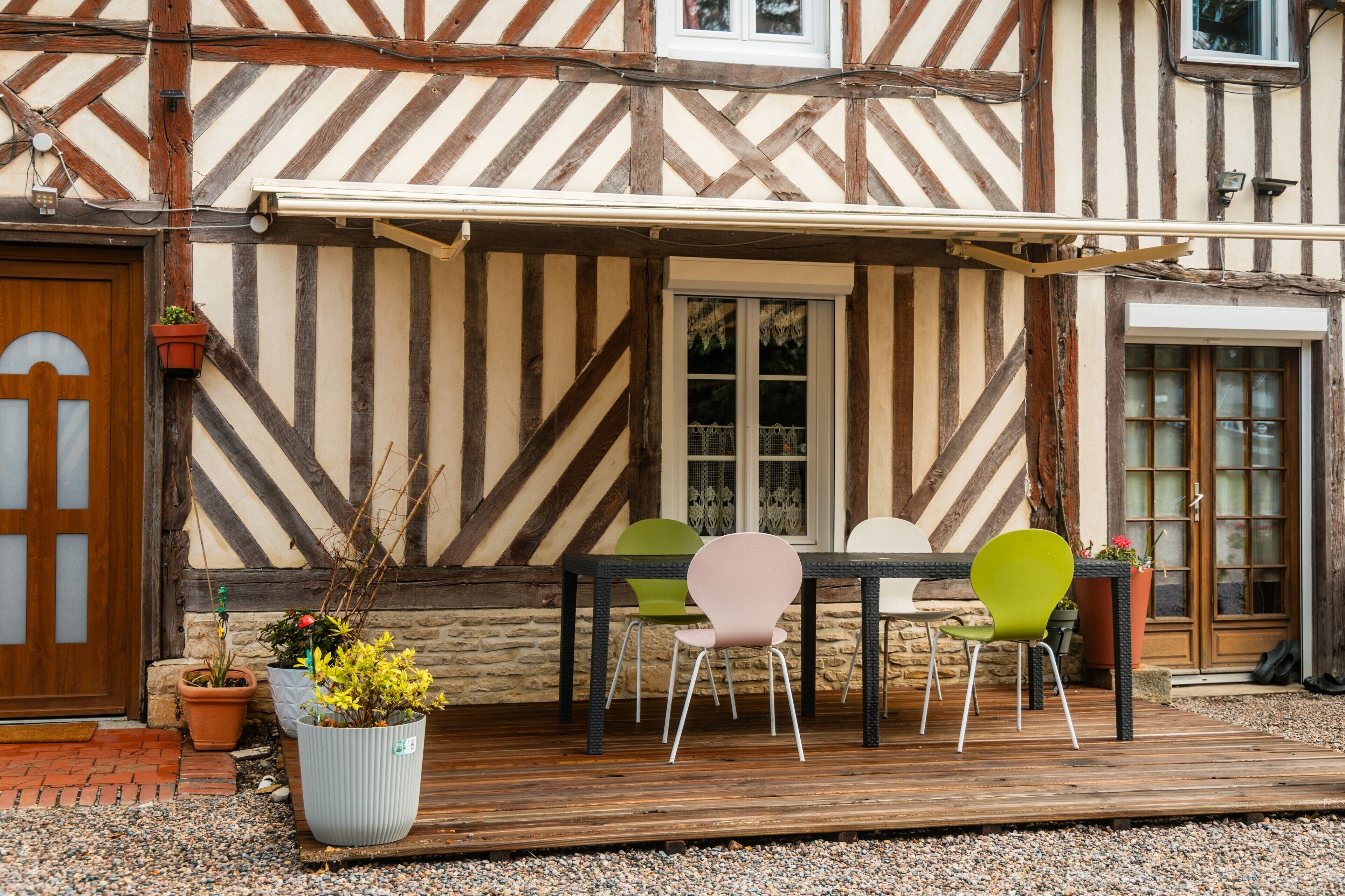 Un bâtiment à colombages doté d’une terrasse en bois, de sièges d’extérieur et de plantes en pot.