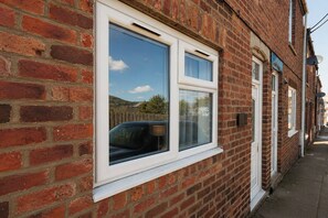 A brick house with a white-framed window, a satellite dish, and a visible number plate. - Spacious 2BR Durham Home for Contractors (Ferryhill)