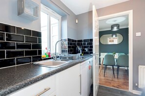 A modern kitchen with black and white tiles, a stainless steel sink, and a dining area with green chairs. - Stylish 3BR | Contractor Friendly | Long Stays (Bearpark)