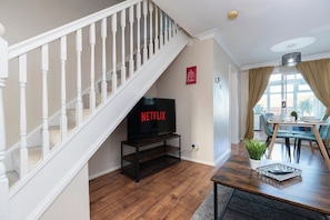 A living room with a wooden staircase, a TV on a stand, a dining table with chairs, and a plant. - Stylish 3BR | Contractor Friendly | Long Stays (Bearpark)