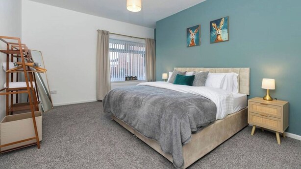 A bedroom with a bed, nightstands, a window with curtains, and two wall art pieces. - Durham 5BR | Contractors & Long Stay Discounts (Murton)