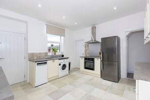 A modern kitchen with a stainless steel refrigerator, a built-in oven, a washing machine, and a window with a view.