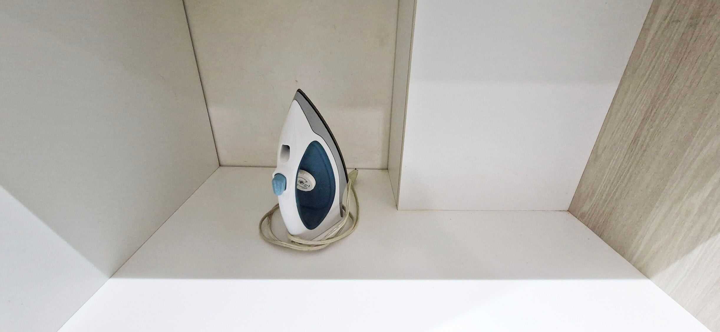 A white ironing board with a blue and white iron in a corner of a room.
