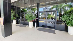 A modern building entrance with large glass doors, potted plants, and a tiled floor. - COCAR0116 - Boulevard Side Residencial (Salvador)