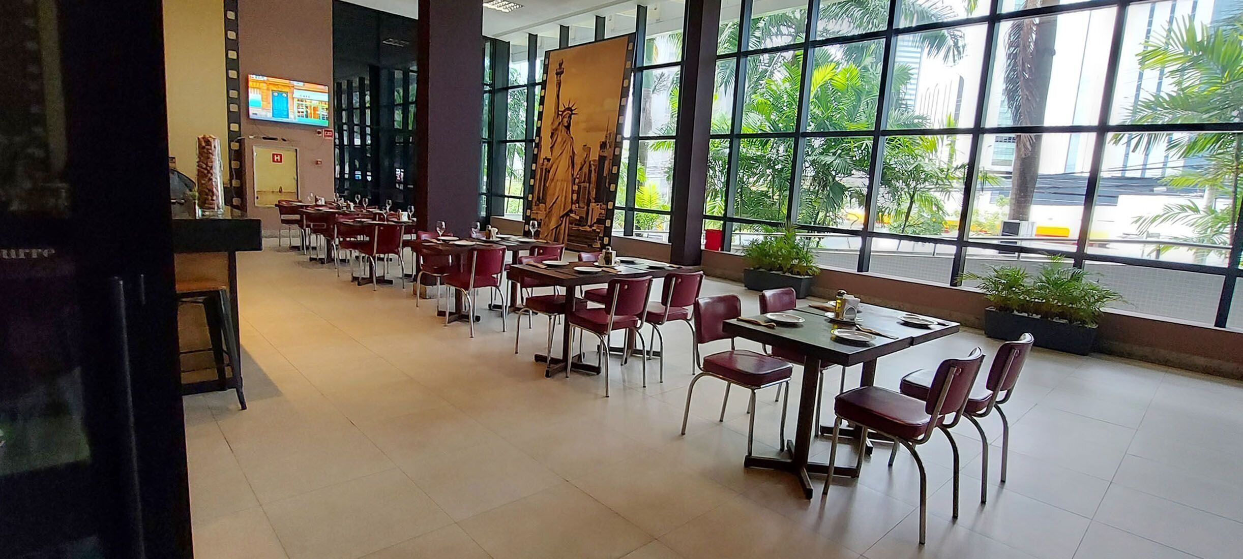 A spacious indoor dining area with tables and chairs, large windows with a view of palm trees, and a statue of the Statue of Liberty.