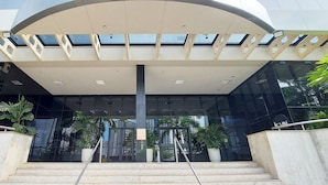 A modern building entrance with a glass facade, a central staircase, and potted plants. - COCAR0116 - Boulevard Side Residencial (Salvador)