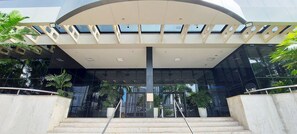 A modern building entrance with a glass facade, a central staircase, and potted plants. - COCAR0116 - Boulevard Side Residencial (Salvador)