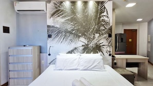 A hotel room with a bed, a desk, an air conditioning unit, and a wall with a palm tree mural. - COCAR0116 - Boulevard Side Residencial (Salvador)