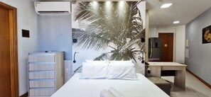 A hotel room with a bed, a desk, an air conditioning unit, and a wall with a palm tree mural. - COCAR0116 - Boulevard Side Residencial (Salvador)