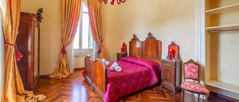 A room with a wooden bed, a red chandelier, a wooden nightstand, and a chair.