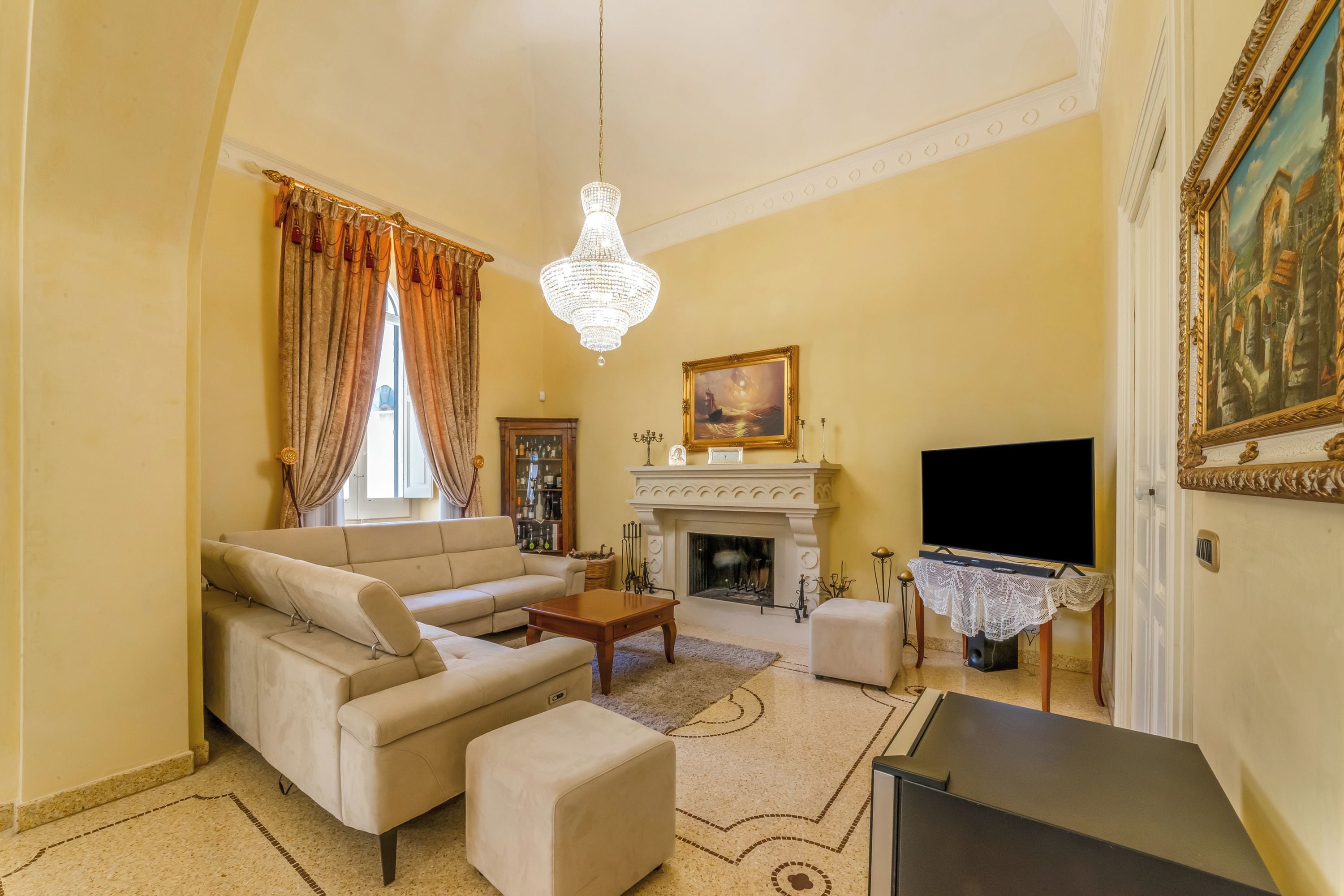 A living room with a sofa, coffee table, fireplace, television, and a chandelier.