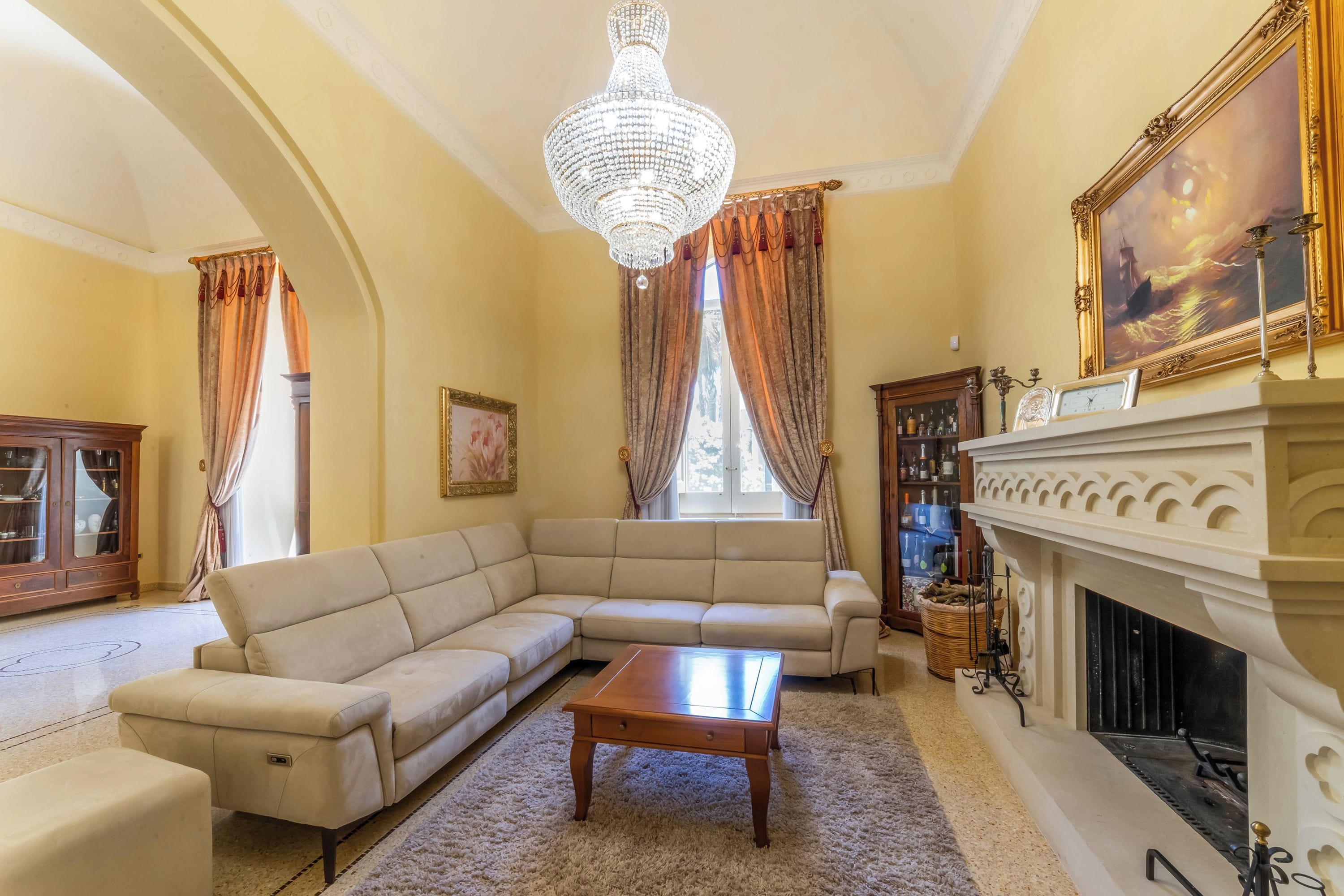 Una sala de estar con un sofá beige modular, una mesa de centro de madera, una chimenea y una araña.