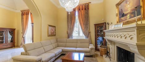 Una sala de estar con un sofá beige modular, una mesa de centro de madera, una chimenea y una araña.