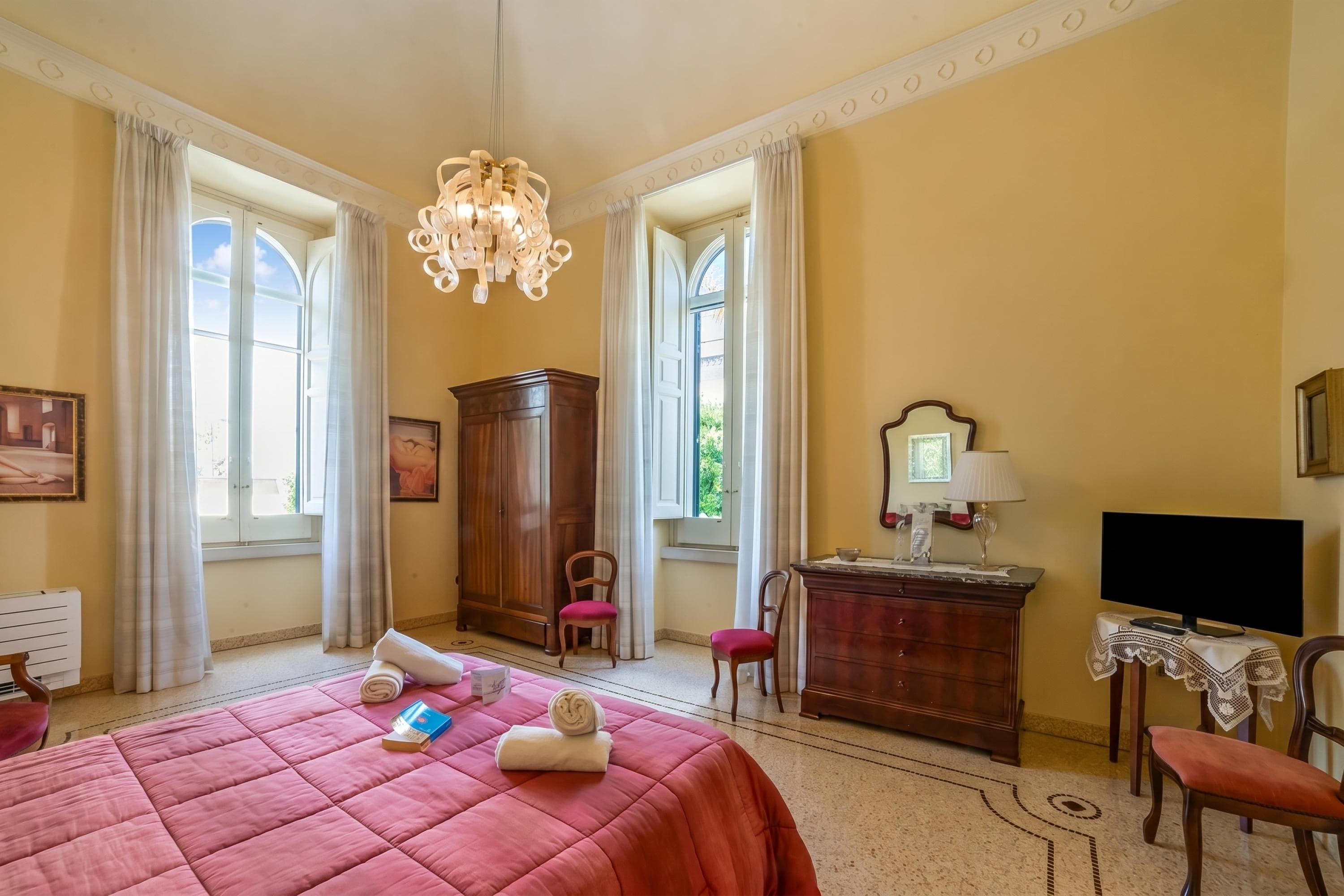 Une chambre d’hôtel avec un lit, un bureau, une chaise, une télévision et un lustre.