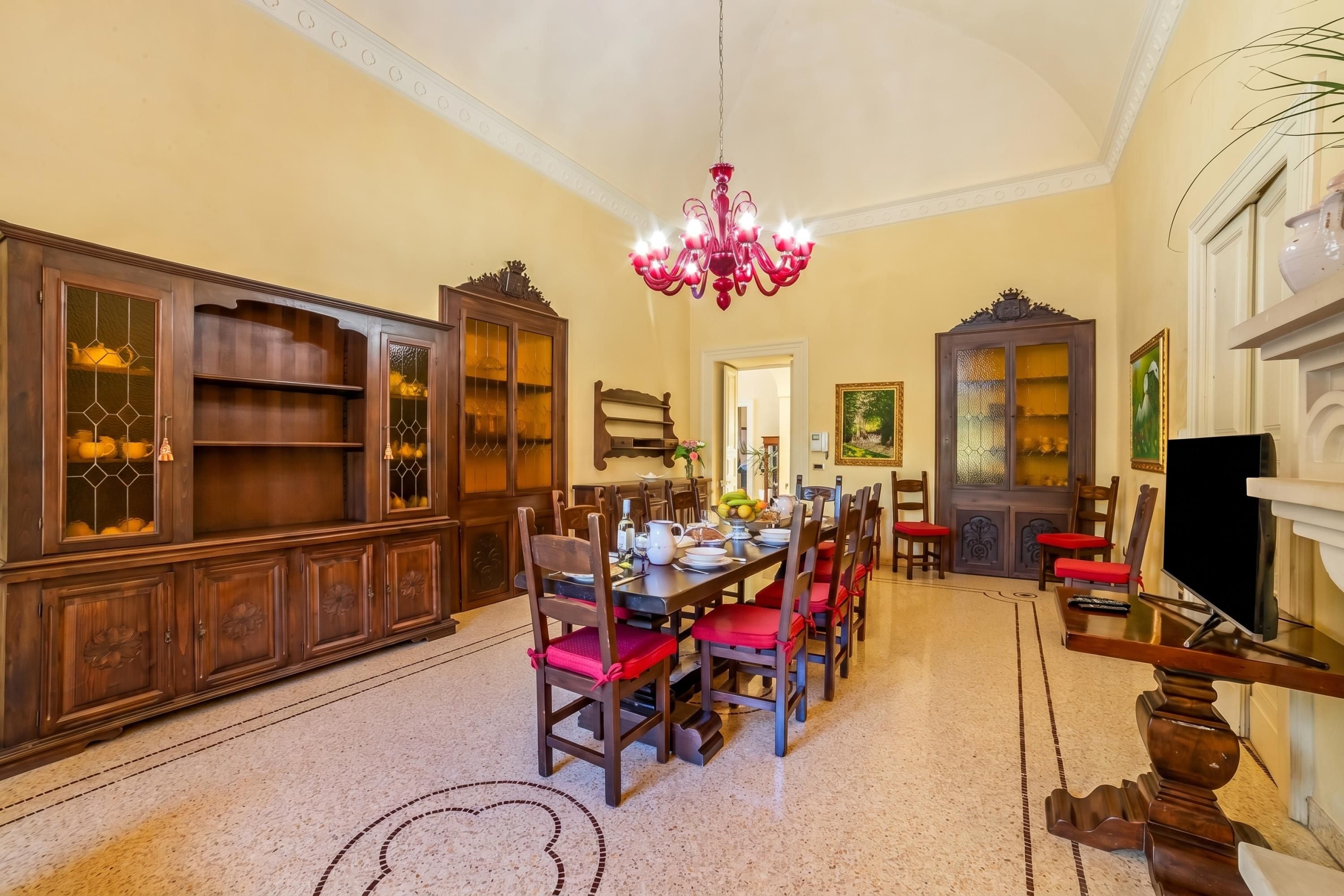 Un comedor con candelabro, armarios de madera y sillas rojas.