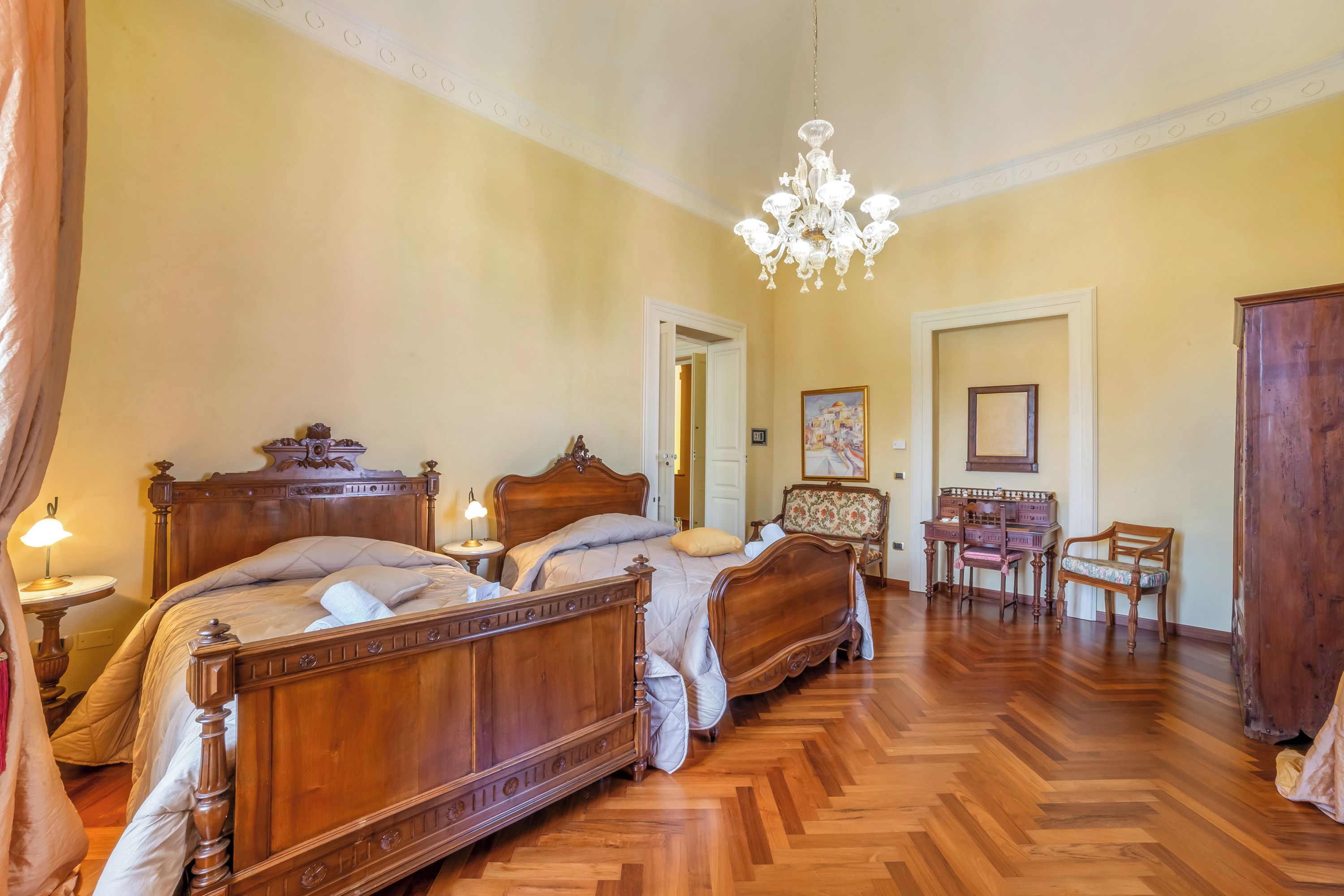 Ein Schlafzimmer mit zwei Holzbetten, einem Kronleuchter, Holzdielen und einem Schreibtisch mit Stühlen.