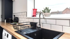 Een keuken met een zwarte spoelbak, een raam met een cactus, en een rode branddeken op de vensterbank.